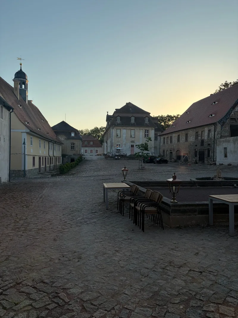 Blick aus dem Hofzimmer über den Schlosshof mit Kopfsteinpflaster und Bouleplatz in der Abenddämmerung
