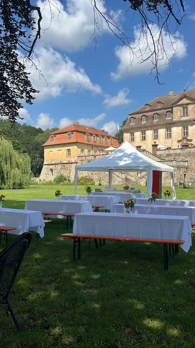 Weiße Festtafeln unter einem Pavillonzelt im Schlosspark vor Schloss Bündorf