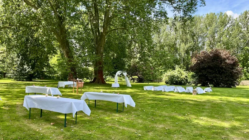 Weiß eingedeckte Tische und Traubogen für eine freie Trauung unter alten Bäumen im Schlosspark Bündorf